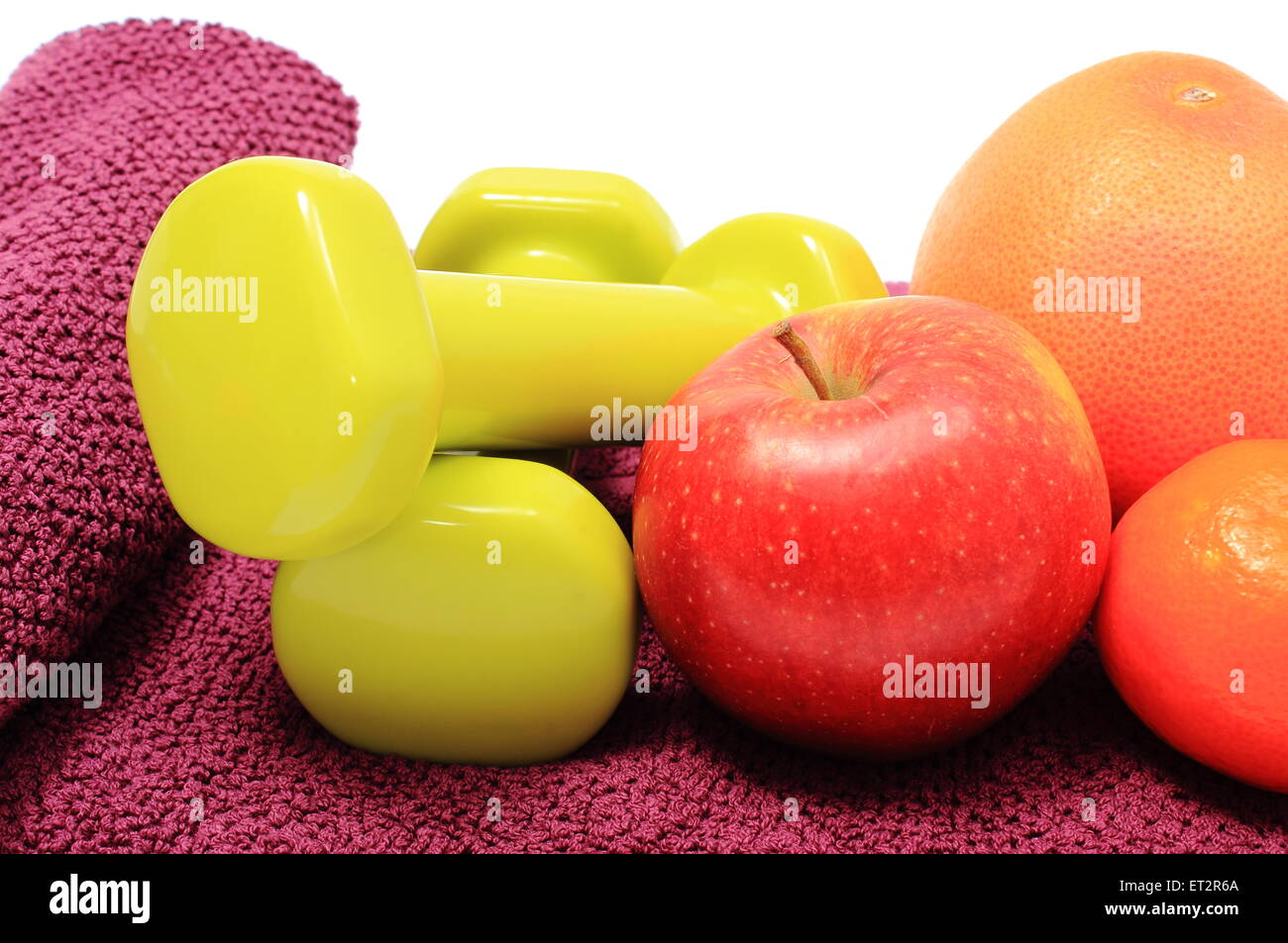 Frisches Obst und grünen Hanteln für den Einsatz in Fitness liegen auf lila Handtuch, Konzept für gesunde Ernährung und Lebensstil Stockfoto