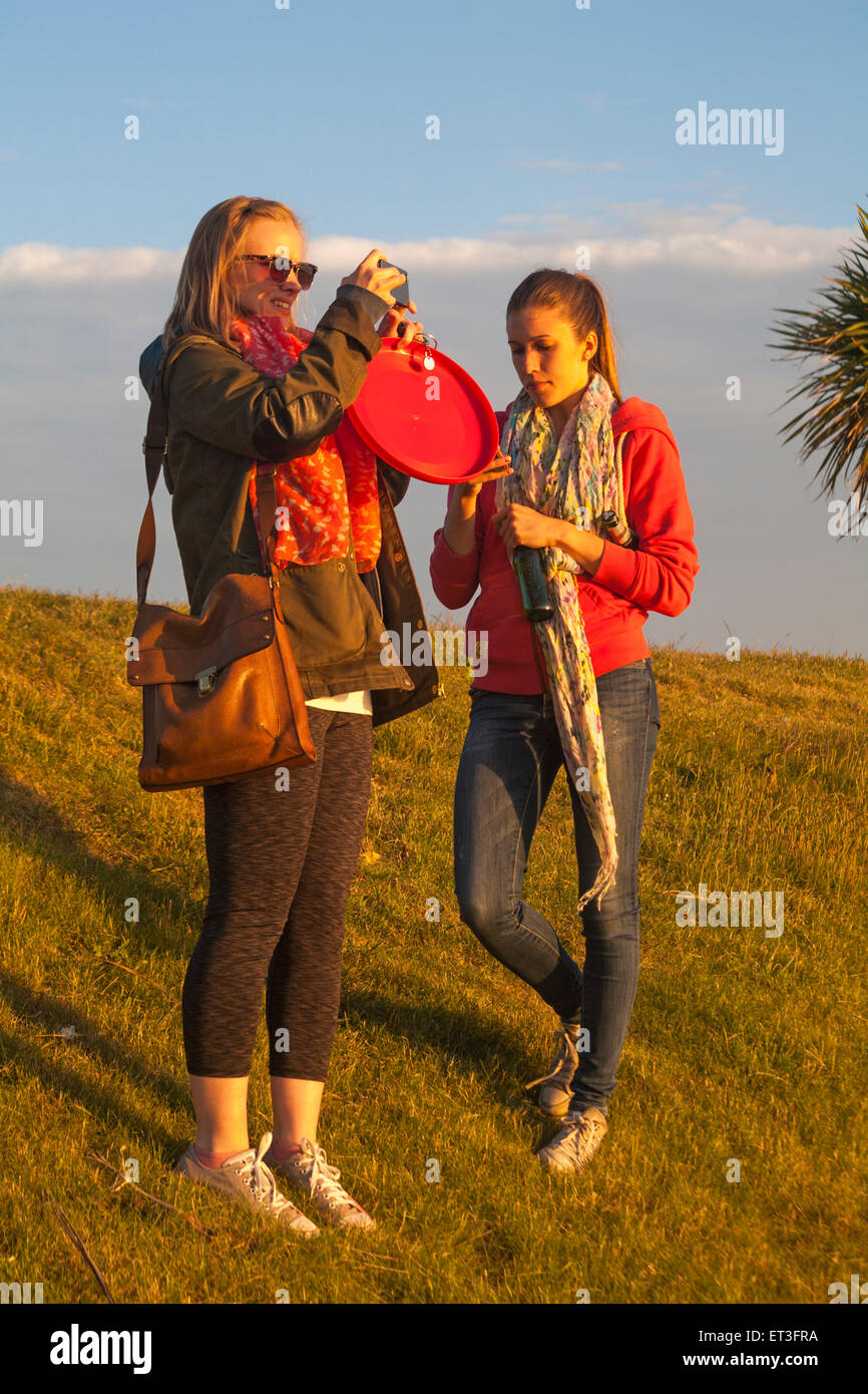 Zwei junge Frauen stehen auf Rasen Bank mit einer Aufnahme eines Fotos der Ansicht auf Sandbänken, Poole, Dorset, Großbritannien im Juni Stockfoto