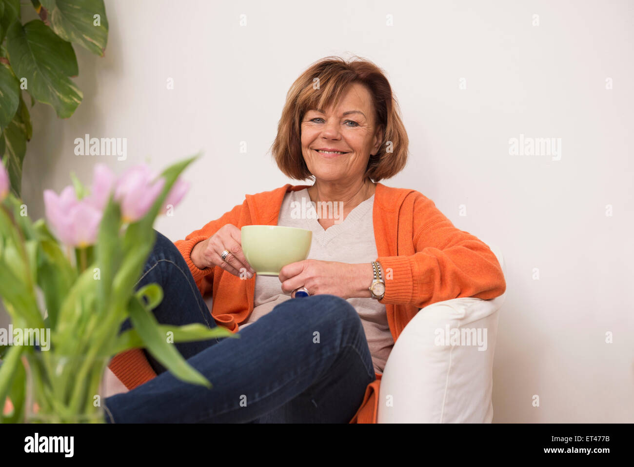 Glückliche ältere Frau auf Sofa sitzen und Tasse Tee zu Hause, Munich, Bavaria, Germany Stockfoto