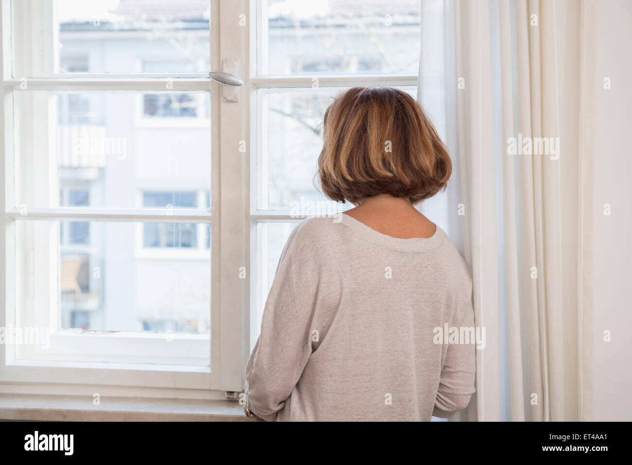 Rückansicht des senior Frau Blick durch ein Fenster, München, Bayern, Deutschland Stockfoto