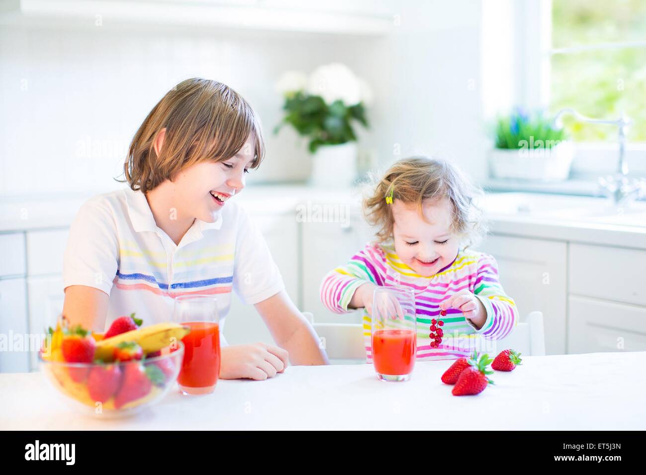 Glücklich Teenager-jungen und seinem Kleinkind Schwester haben Obst und Müsli mit Erdbeeren zum Frühstück vor der Schule und kindergarten Stockfoto