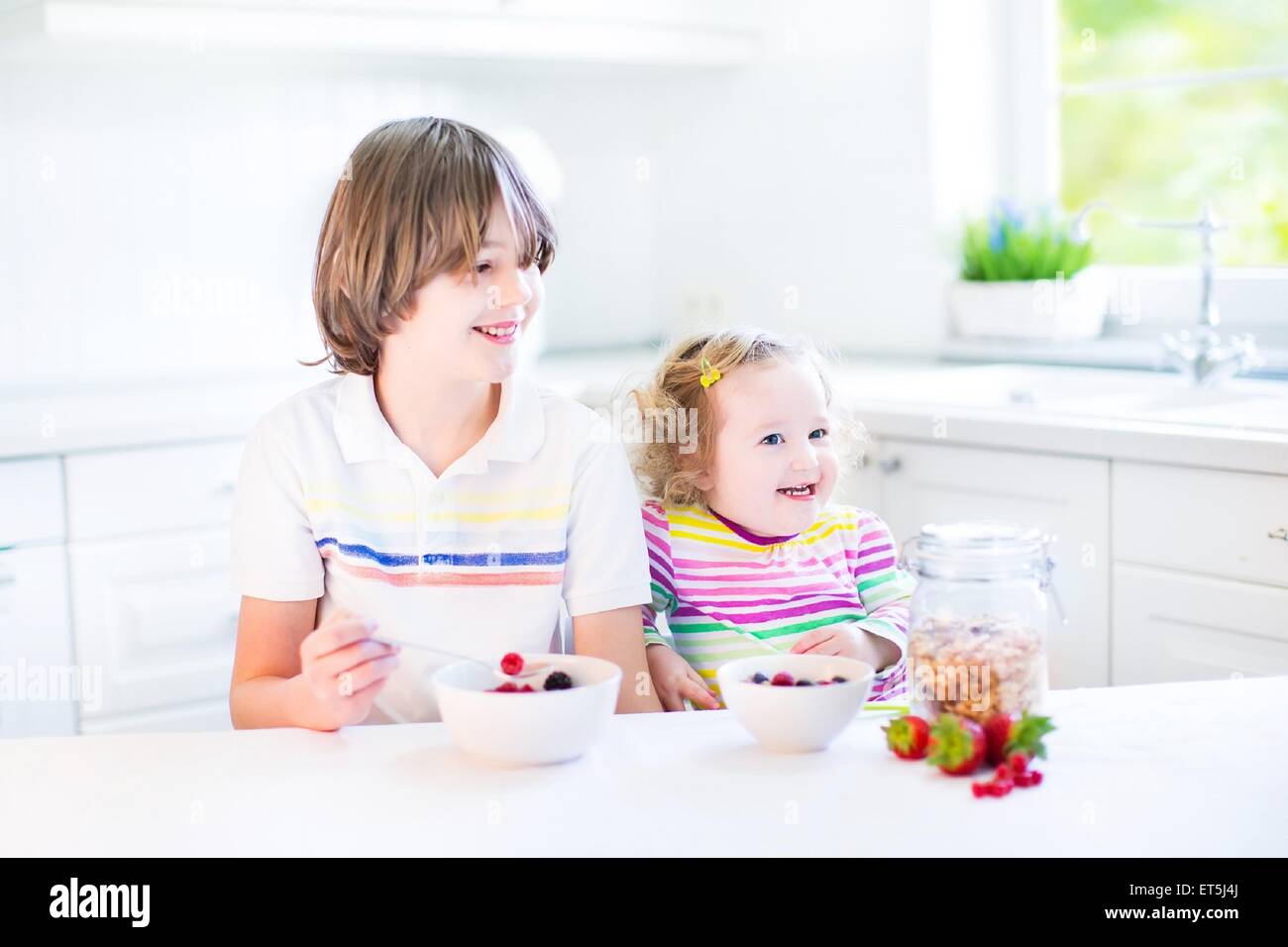 Glücklich Teenager-jungen und seinem Kleinkind Schwester haben Obst und Müsli mit Erdbeeren zum Frühstück vor der Schule und kindergarten Stockfoto