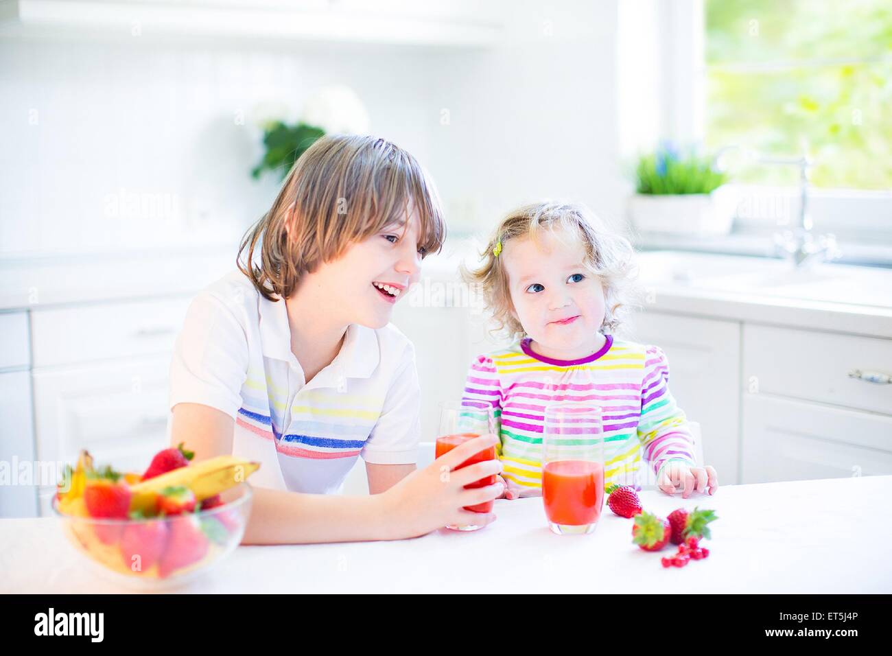 Glücklich Teenager-jungen und seinem Kleinkind Schwester haben Obst und Müsli mit Erdbeeren zum Frühstück vor der Schule und kindergarten Stockfoto