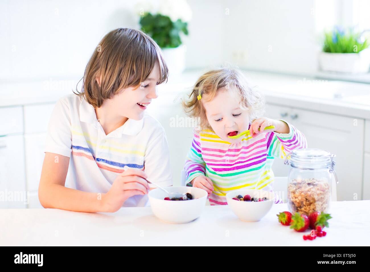 Glücklich Teenager-jungen und seinem Kleinkind Schwester haben Obst und Müsli mit Erdbeeren zum Frühstück vor der Schule und kindergarten Stockfoto