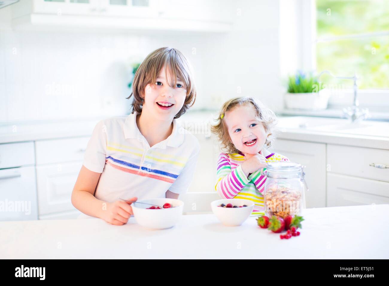 Glücklich Teenager-jungen und seinem Kleinkind Schwester haben Obst und Müsli mit Erdbeeren zum Frühstück vor der Schule und kindergarten Stockfoto