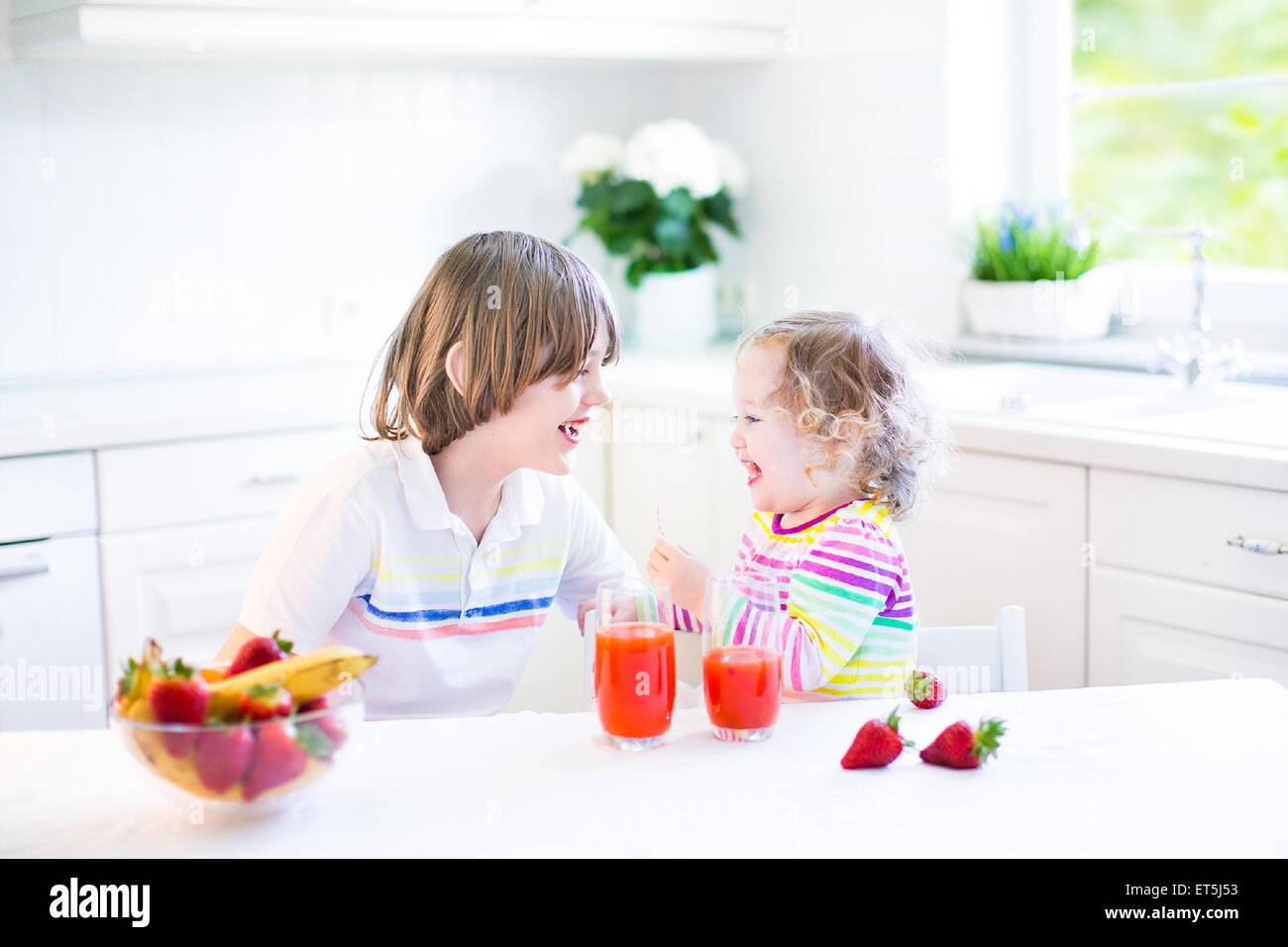 Glücklich Teenager-jungen und seinem Kleinkind Schwester haben Obst und Müsli mit Erdbeeren zum Frühstück vor der Schule und kindergarten Stockfoto
