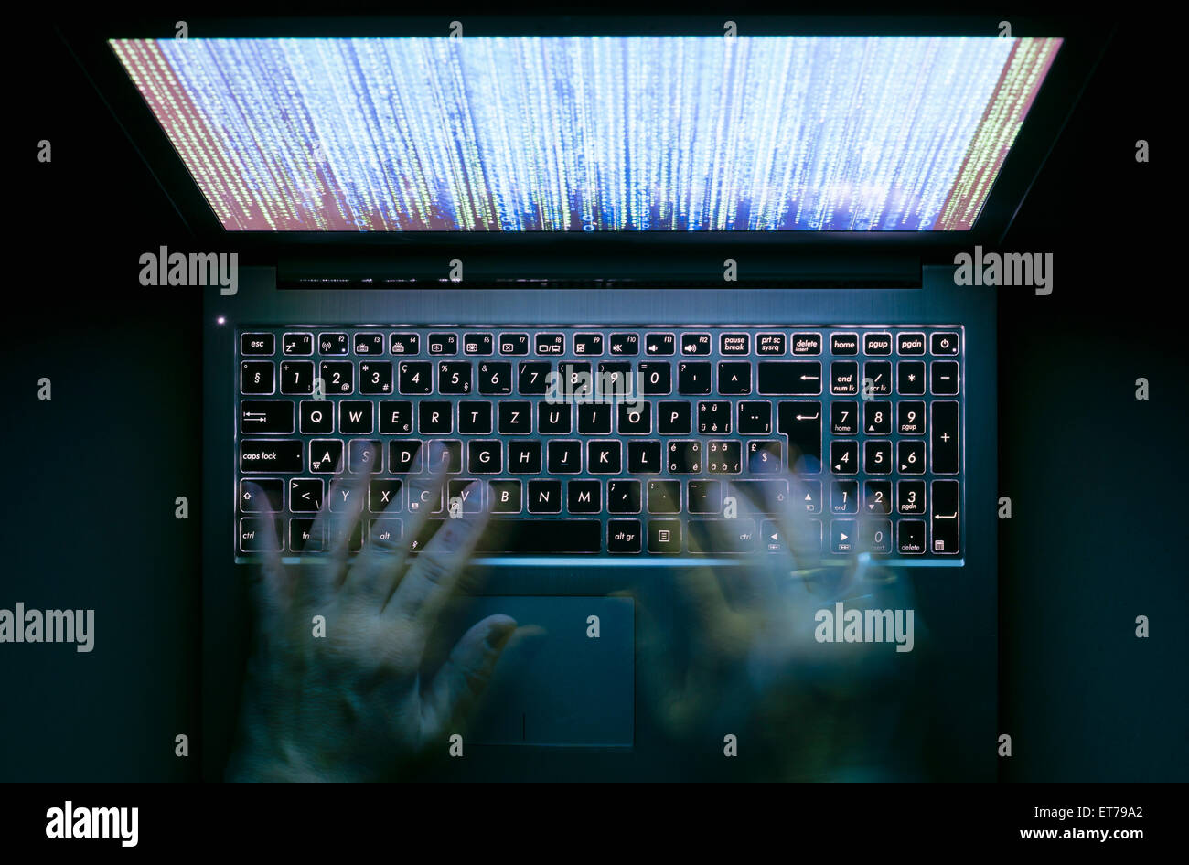 Hände werden auf einem Laptop-Computer in der Dunkelheit mit beleuchtete Tastatur und mystische Programmcode auf dem Bildschirm tippen. Stockfoto