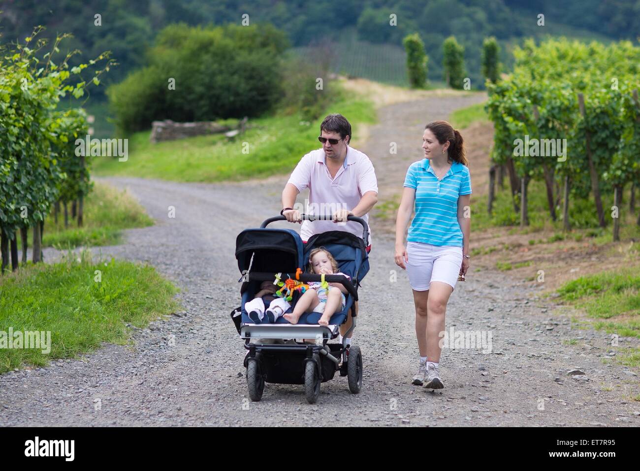 Junge aktive Eltern Wandern in den Bergen mit einem double Twin Kinderwagen mit zwei Kindern, Bruder und Schwester Stockfoto