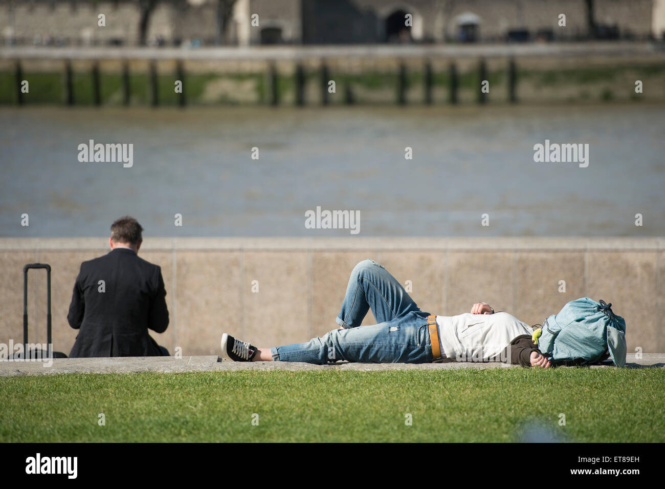 Touristen, die ein Nickerchen an einem sonnigen Tag an der Themse in London Stockfoto