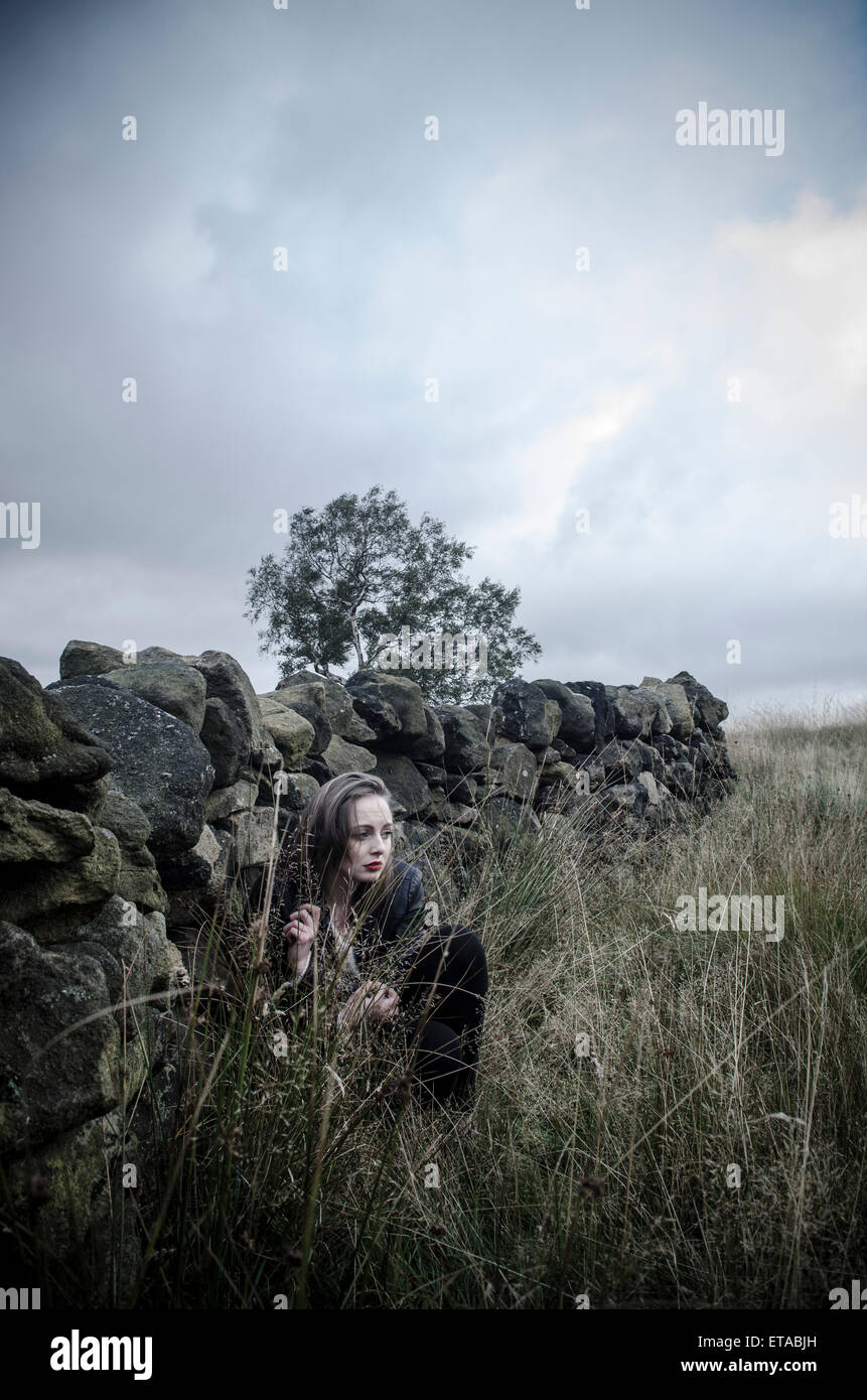 Angst junge Frau versteckt sich hinter einer Trockensteinmauer Stockfoto