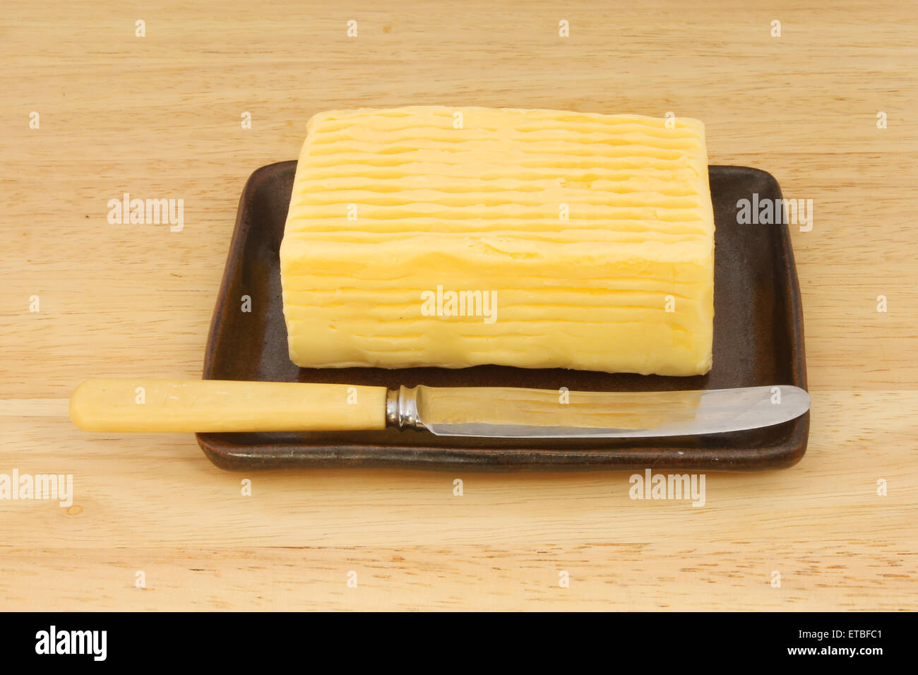 Block von Butter mit einem Messer in einer Schale auf einem Holzbrett Stockfoto
