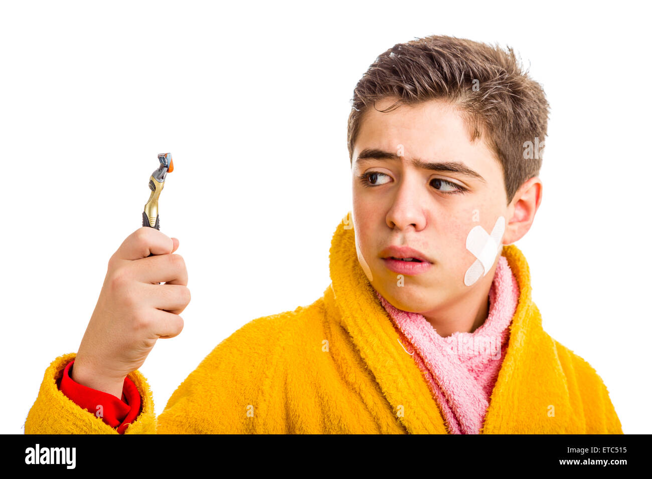 Ein spanischer Junge trägt einen gelben Bademantel mit einem rosa Handtuch um den Hals: er hat einige Flecken im Gesicht und starrt auf das Rasiermesser er für die Rasur verwendet Stockfoto