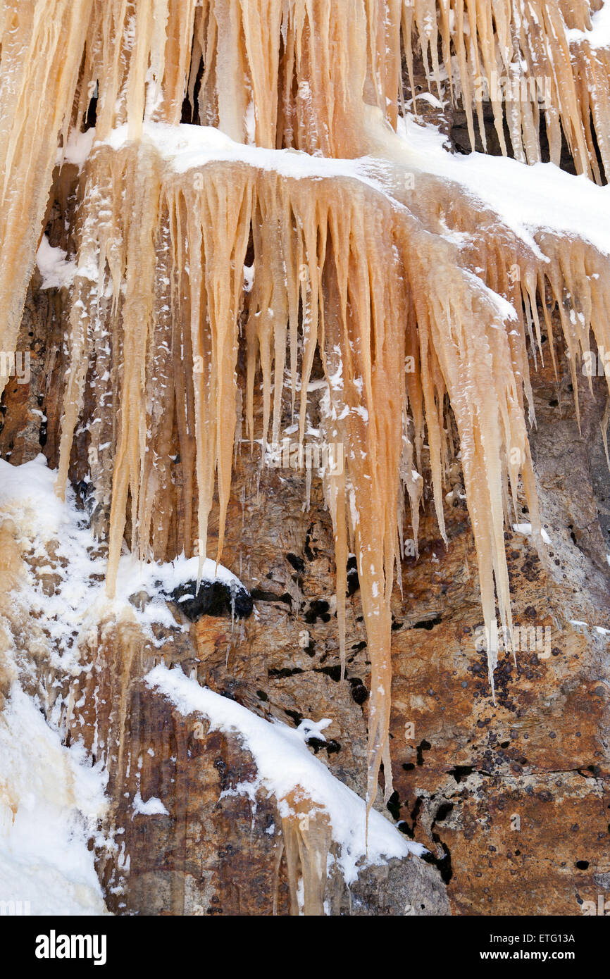 Langen, spitzen Eiszapfen hängen von einer Felswand sind farbig Orange von Eisenoxid im Boden. Stockfoto