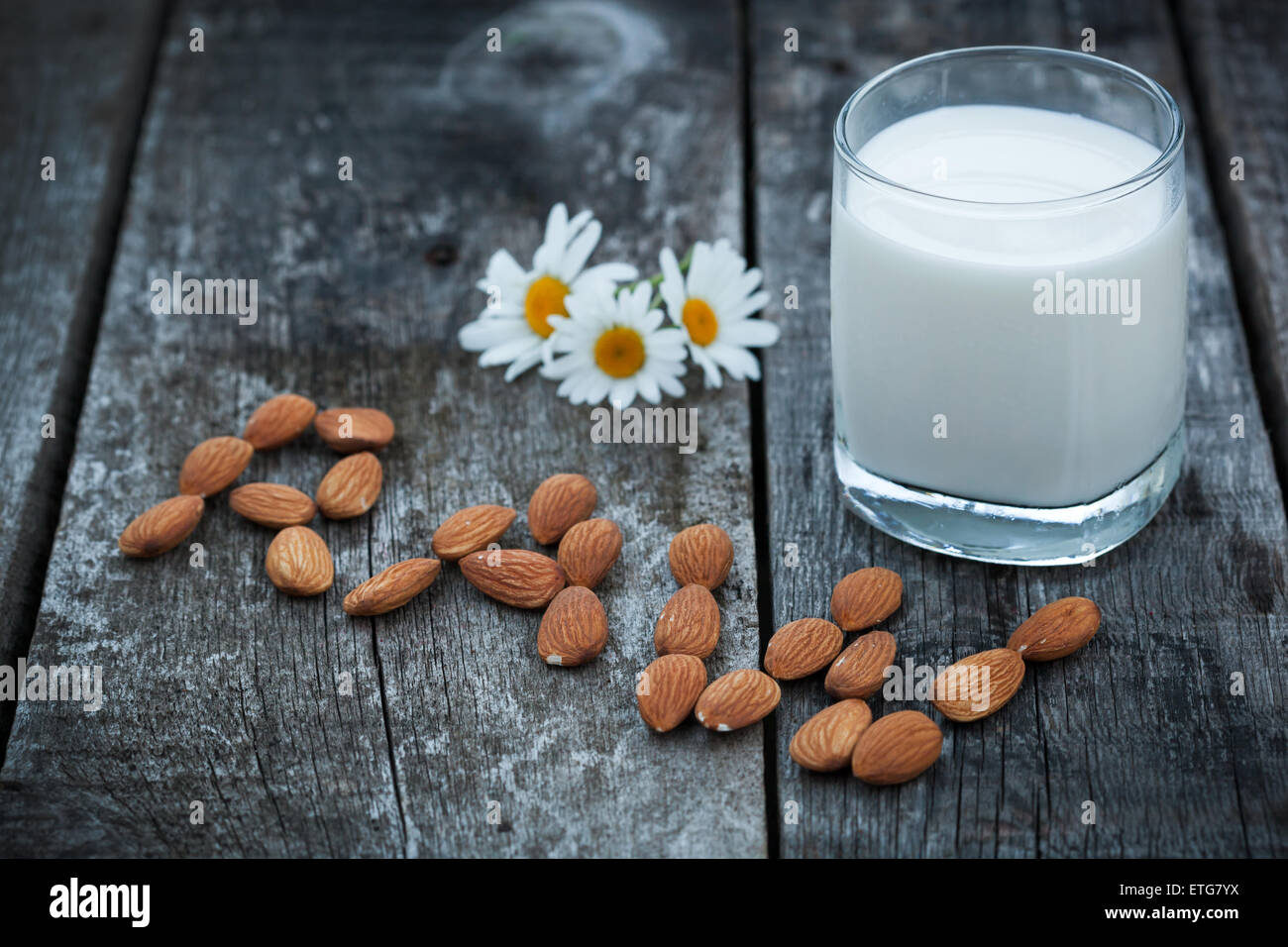 Glas Bio Mandelmilch auf Holztisch mit Wort "Roh", dekoriert frische Kamille-Blüten. Gesunde Ernährung-Konzept, Selective Stockfoto