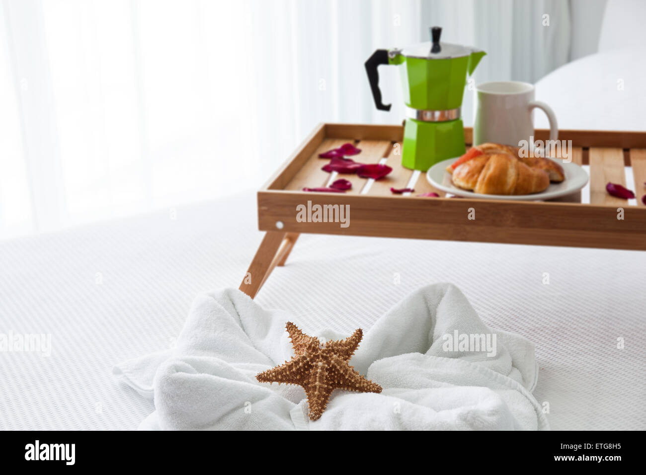 Frühstück Holztablett mit Kaffeemaschine und ein Croissant auf Bett, dekorierte Seestern auf weißen Handtuch Stockfoto