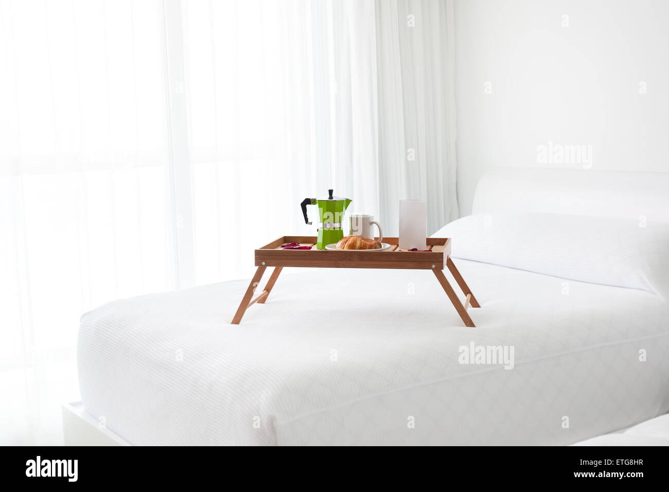 Frühstück Holztablett mit Kaffeemaschine, weiße leere Karte und Croissant auf Bett. Licht vom Fenster im Zimmer Stockfoto