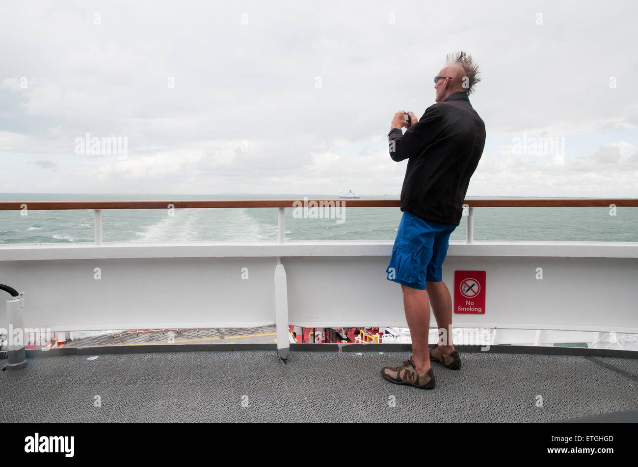 Mann in Shorts und Mohikaner Haarschnitt auf Fähre nimmt Bilder mit Digitalkamera, Ärmelkanal Calais-Dover Stockfoto