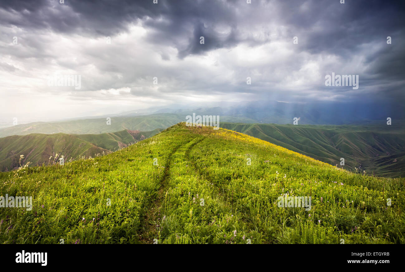 Wiese mit Auto Track und Bergen am dramatischen bedecktem Himmel in Ushkonyr in der Nähe von Chemolgan, Kasachstan, Zentralasien Stockfoto