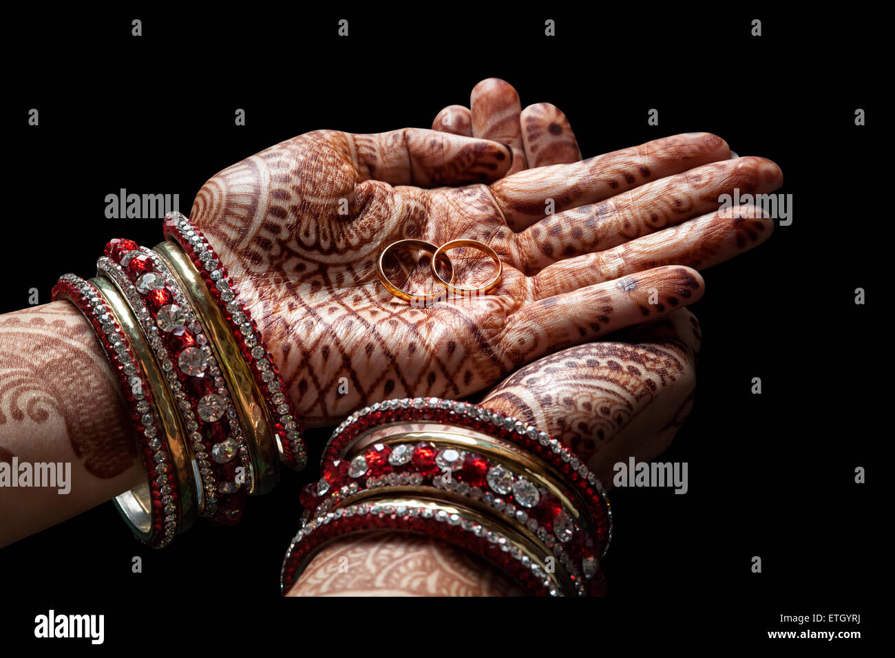 Frau Hände mit Henna halten zwei goldene Hochzeit Ringe auf schwarzem Hintergrund Stockfoto