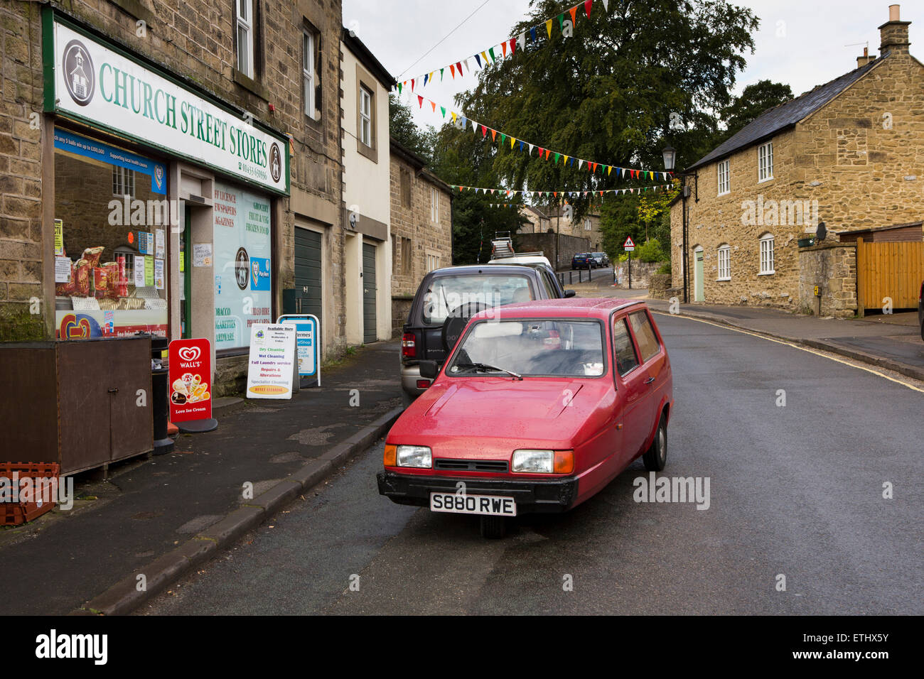 Großbritannien, England, Derbyshire, Eyam, Church Street, schlechte Parkmöglichkeiten, alte Reliant Robin bellte blockieren Straße vor Laden Stockfoto