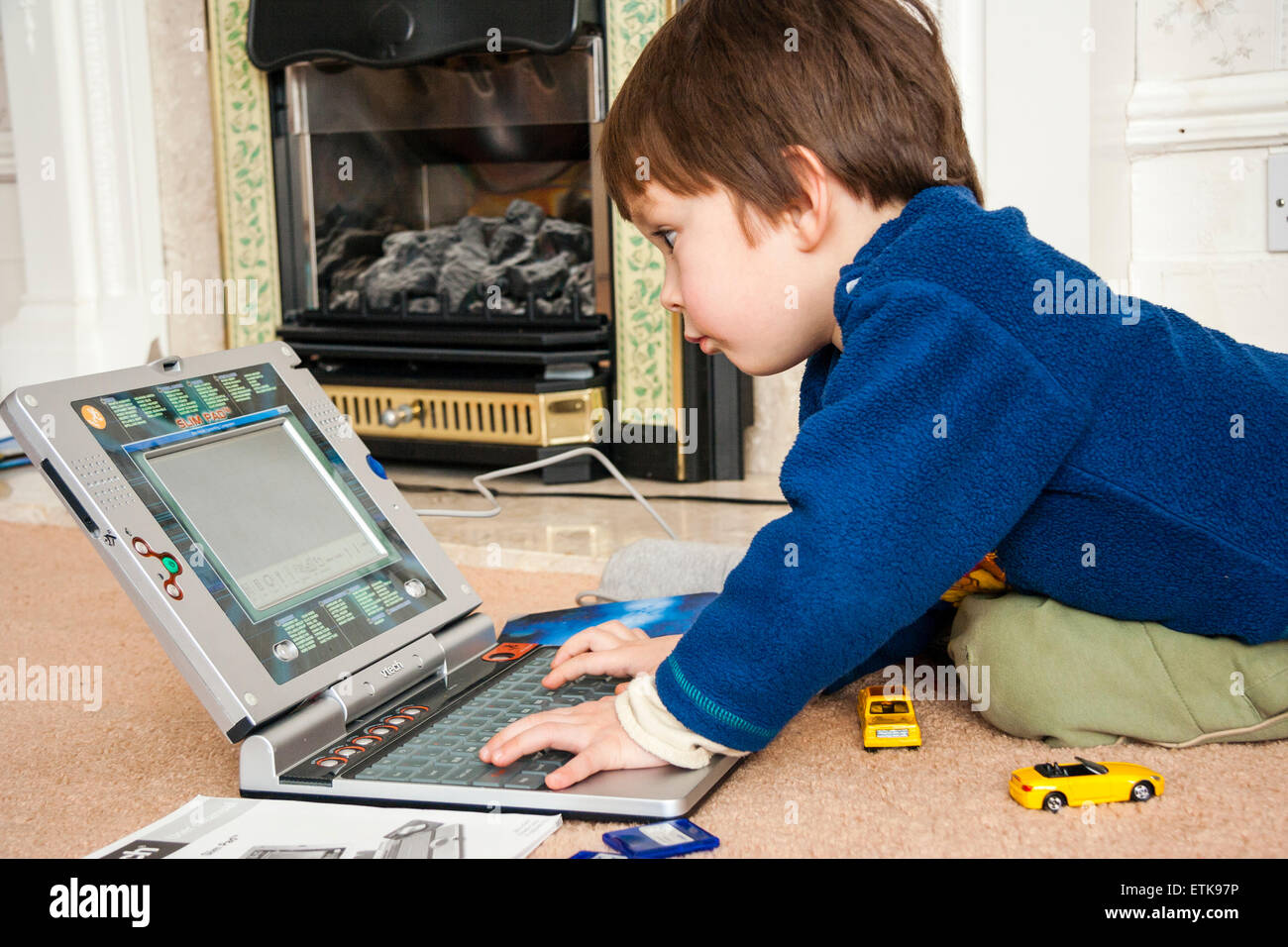 Junges Kind, Junge, 3-4 Jahre alt, drinnen kniend auf Teppich, konzentriert zu Spielen der Kinder mit V-Tech laptop computer, lernen grundlegende computering Fähigkeiten Stockfoto