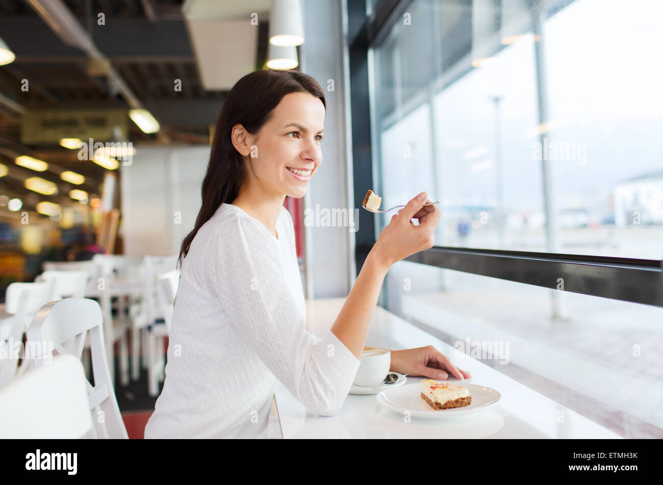 lächelnde junge Frau mit Kuchen und Kaffee im café Stockfoto