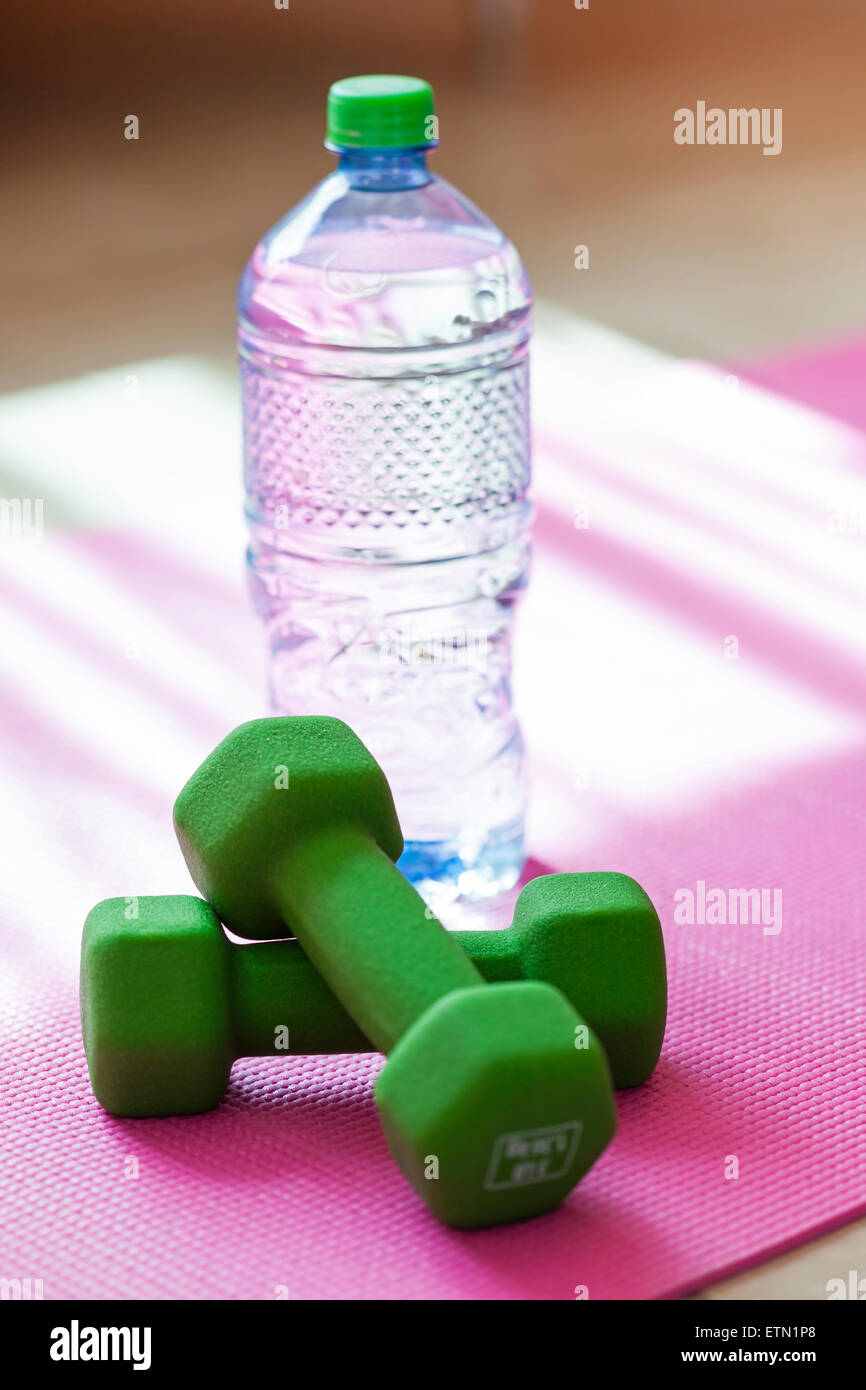 Zwei Kurzhanteln mit Mineralwasser auf Yoga-Matte, sportlichen Lifestyle-Konzept Stockfoto