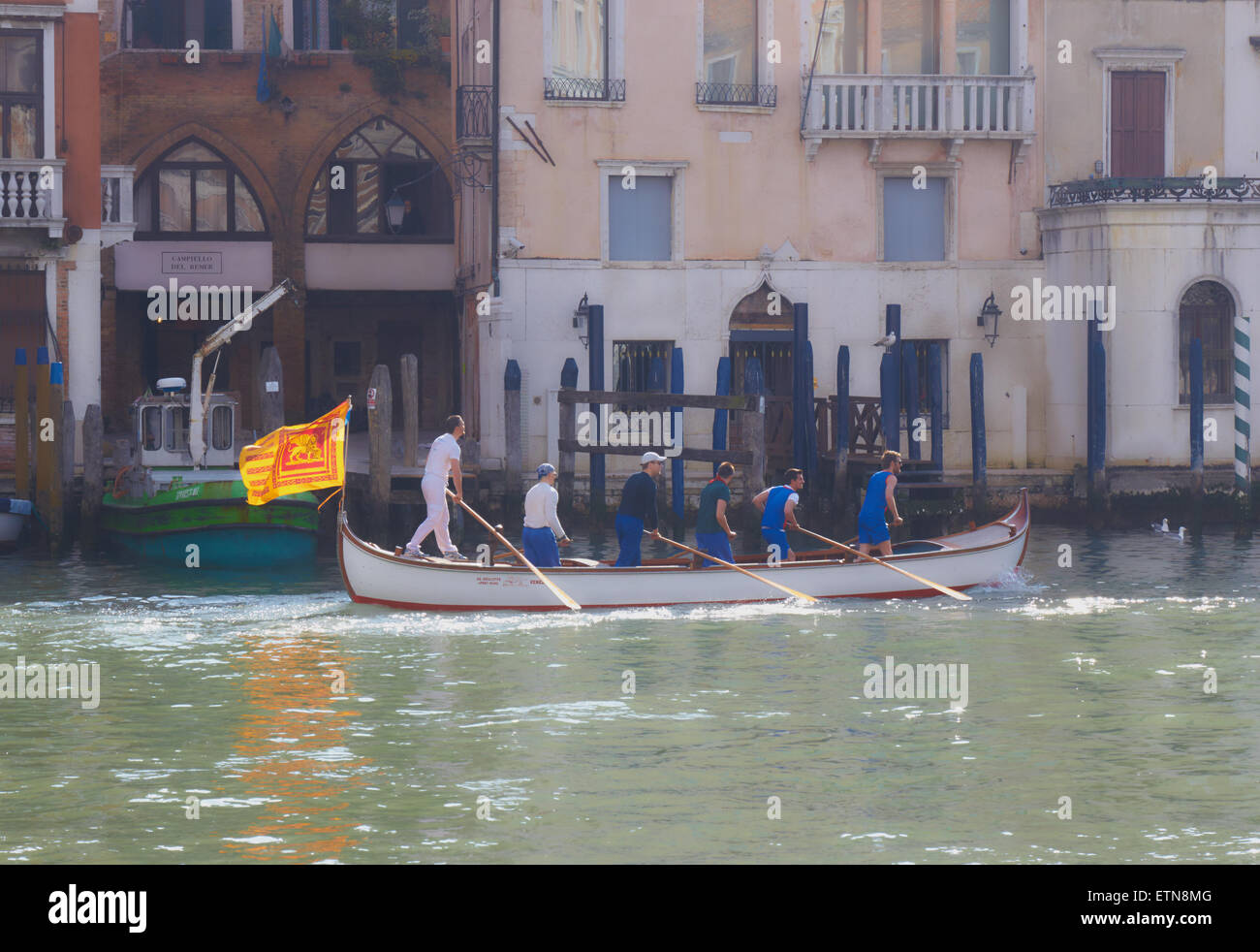 Trübe Sonnenlicht auf einem Boot ruderte von sechs Männern und die venezianischen Flagge eines geflügelten Löwen Reisen entlang des Canal Grande Venedig Stockfoto