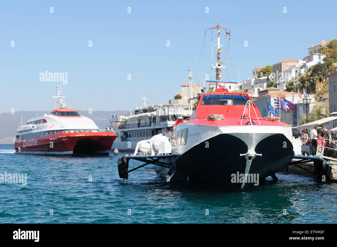 Eine Katamaran-Fähre nähert sich seinen Liegeplatz neben einem festgemachten Tragflächenboot im Hafen von Hydra, Saronische Inseln, Griechenland Stockfoto