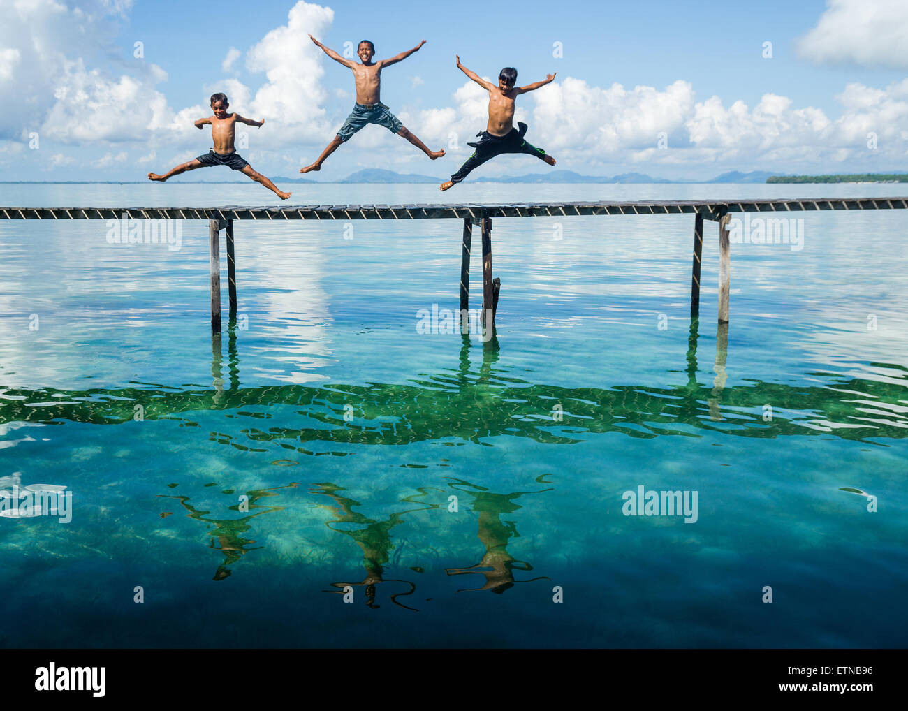 Drei Jungs springen zum Meer von einer Anlegestelle Salakan Insel, Semporna, Sabah, Malaysia Stockfoto