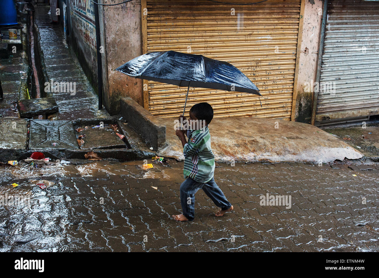 Ein kleiner Junge mit Regenschirm im Monsun-Regen in Mumbai, Indien Stockfoto