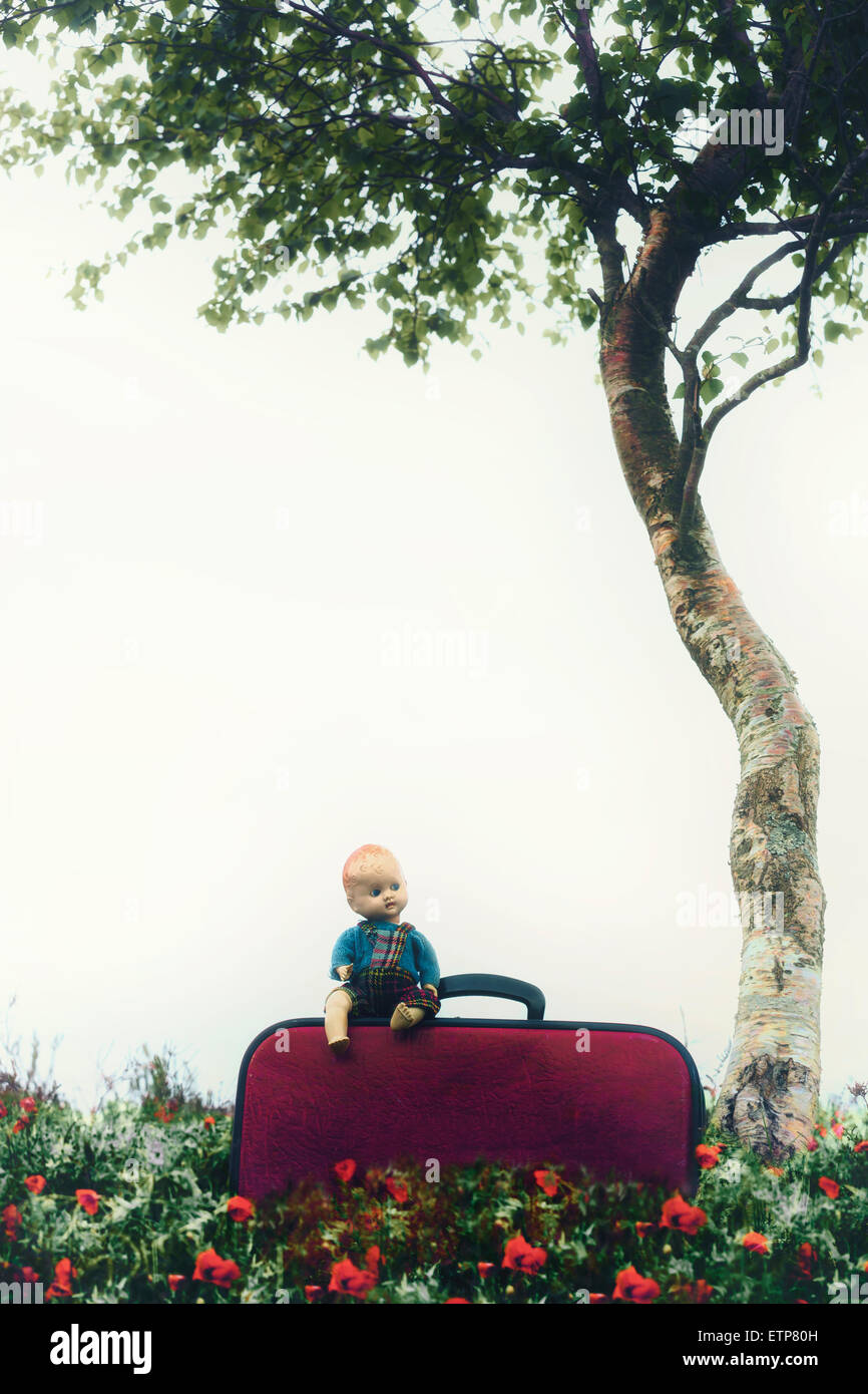 eine alte Puppe sitzt auf einem roten Koffer Stockfoto