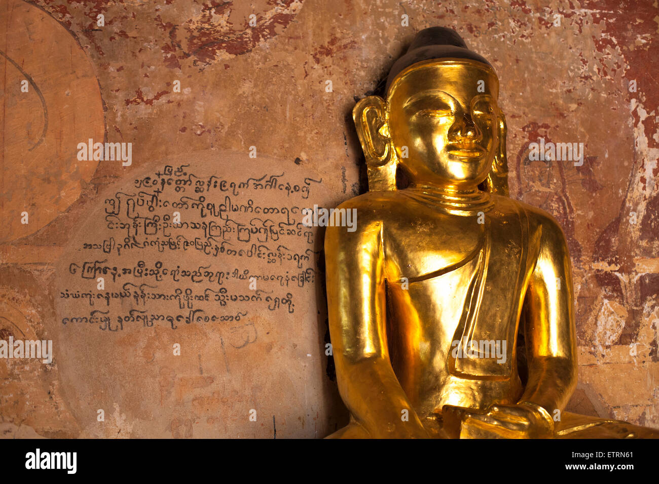 Goldene Buddha-Statue vor der birmanischen Schrift an Wand, Bagan, Myanmar Stockfoto