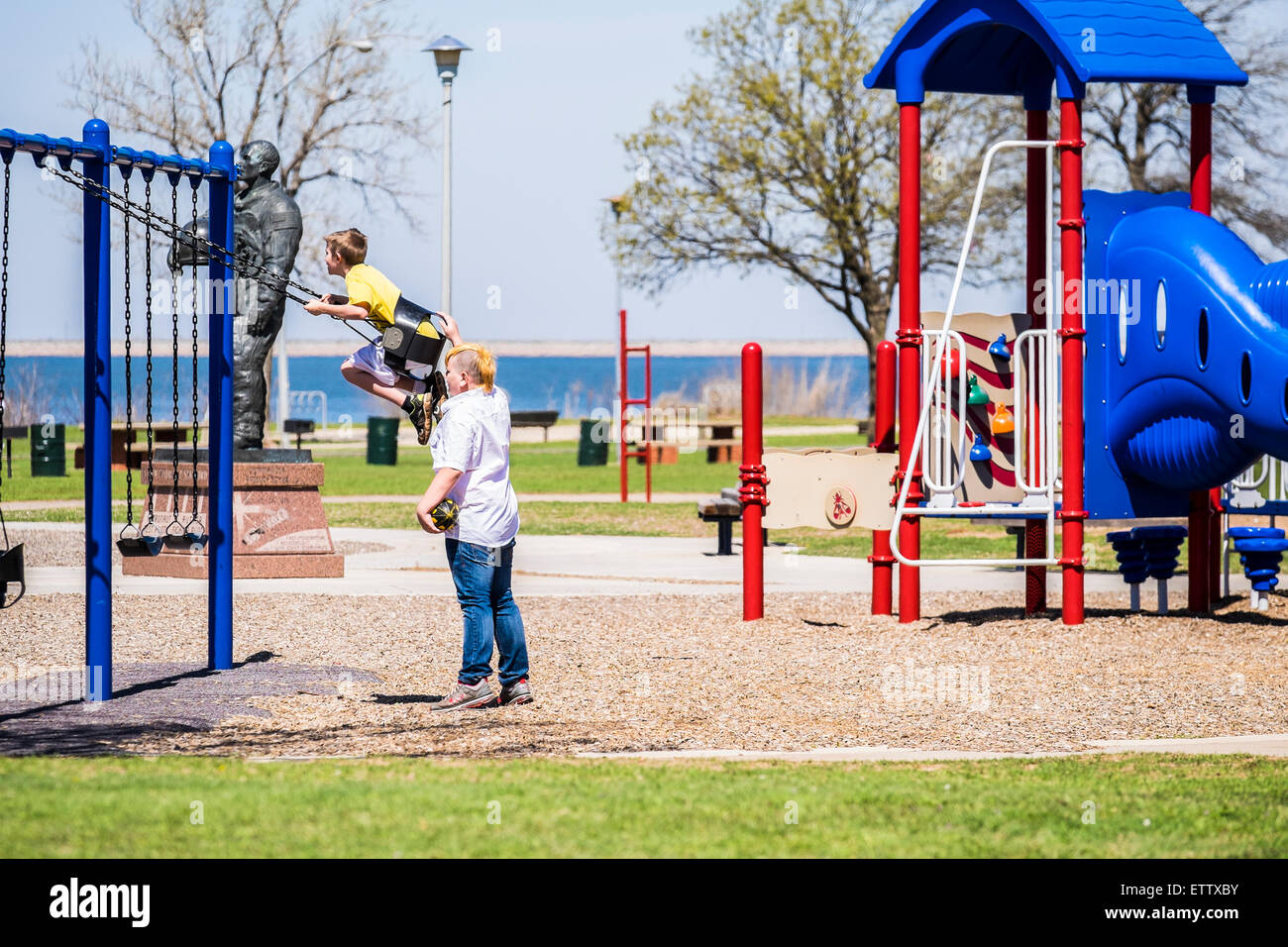 Ein Teenager mit einem funky Haarschnitt schwingt einen jüngeren Jungen auf einem öffentlichen Spielplatz. Oklahoma City, Oklahoma, USA. Stockfoto