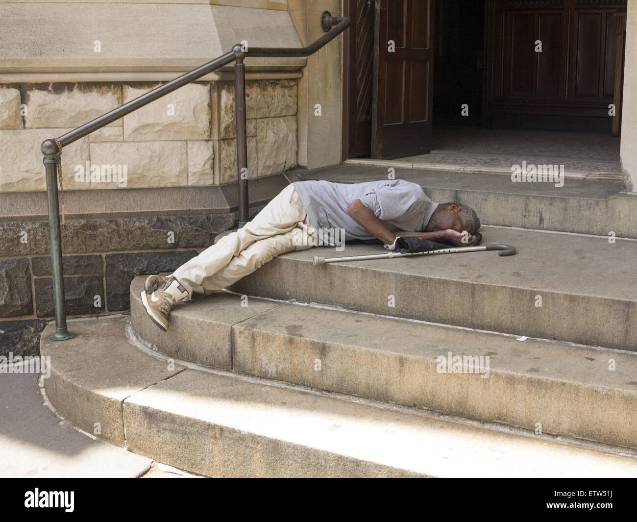 Mann mit einem Stock schläft auf den Stufen einer christlichen Kirche an der 7th Avenue in Park Slope, Brooklyn, NY. Stockfoto