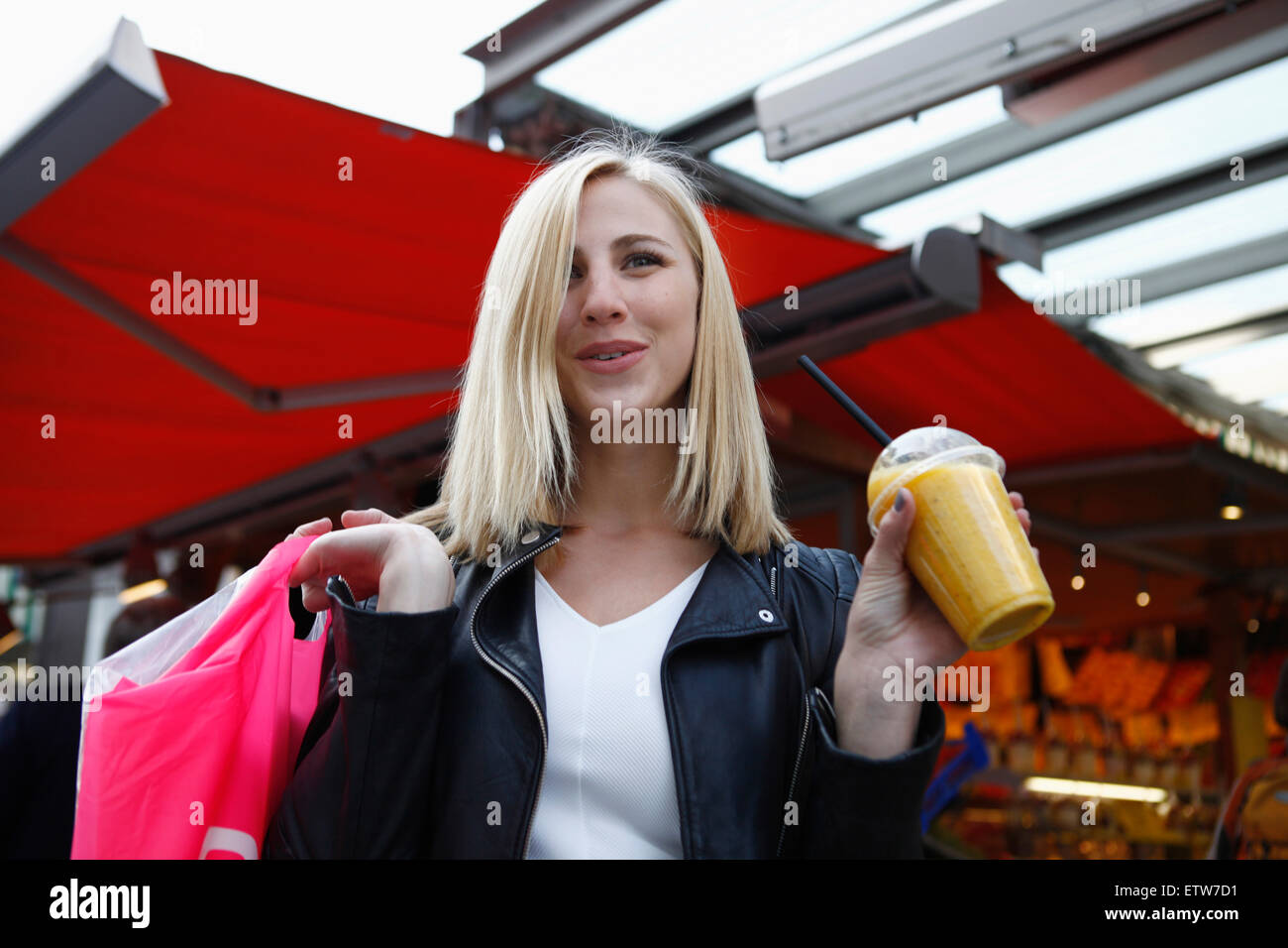 Lächelnde blonde Frau mit Einkaufstasche mit Kunststoff-Tasse Orangensaft Stockfoto