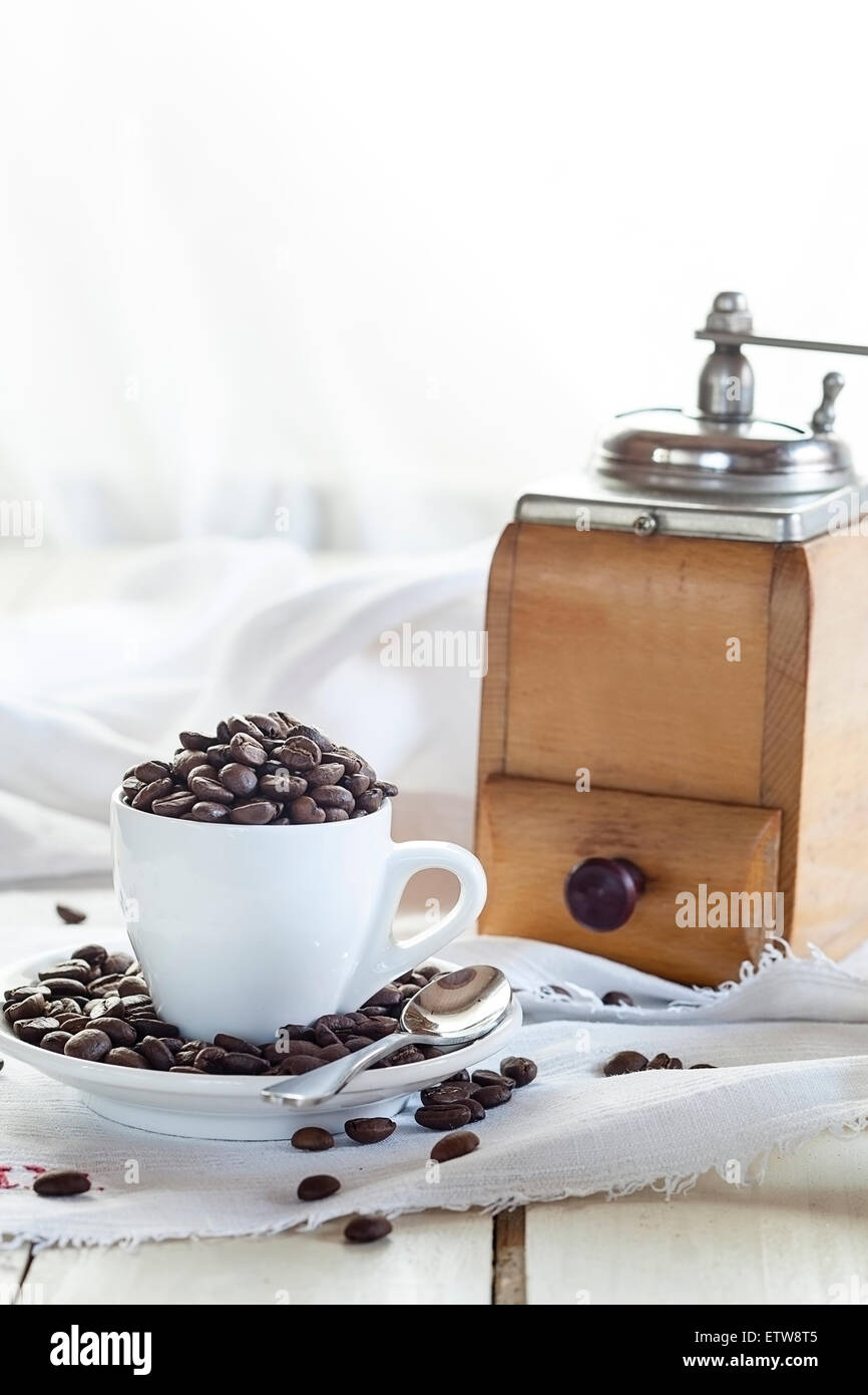 Alte Kaffeemühle und Kaffeetasse mit Kaffeebohnen gefüllt Stockfoto