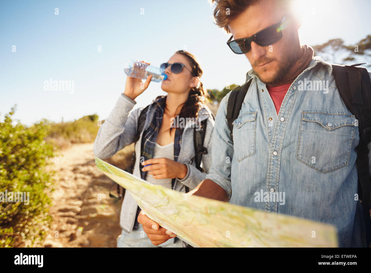 Paar auf Land gehen gemeinsam, Sommerurlaub in Landschaft. Junger Mann Kartenlesen während Frau Trinkwasser in Zeitmessung Stockfoto