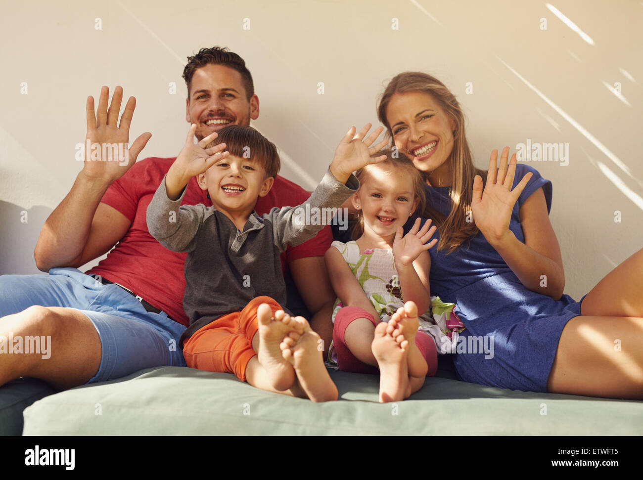 Familie sitzt auf couch lächelnd und gemeinsam lachen, winken in die Kamera. Paar mit Kinder auf Terrasse Spaß im Freien in ihrer Stockfoto