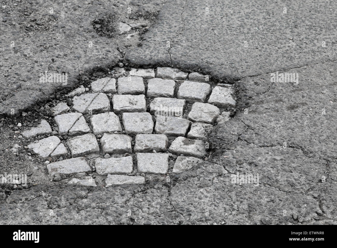 Schlagloch mit alten grauen Steinpflaster auf beschädigten städtischen Asphaltstraße Stockfoto