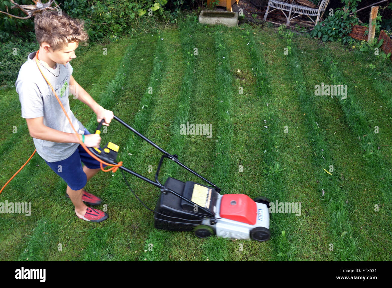 Berlin, Deutschland, junge mäht den Rasen in einem Garten