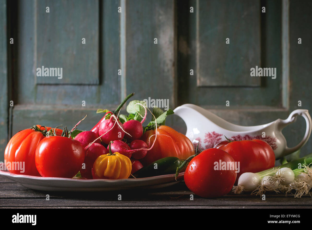 Haufen von Frischgemüse reif bunte Tomaten, Chilischoten, Frühlingszwiebeln und Bündel Radieschen auf Vintage Platte und Porzellan g Stockfoto