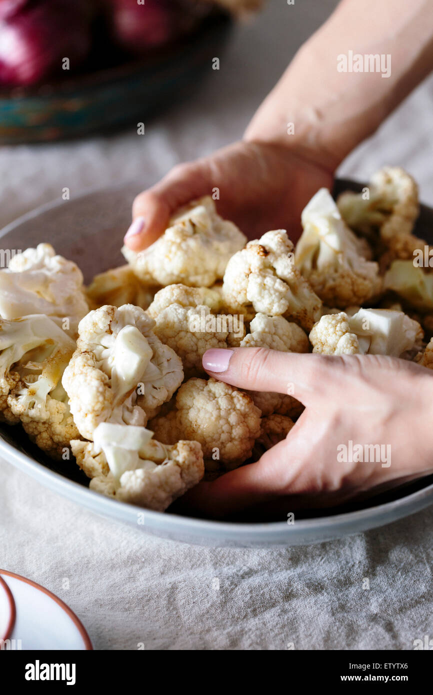 Eine Frauenhand sind Incorprating einem würzigen Dressing auf frisch geschnittenem Blumenkohlröschen. Stockfoto