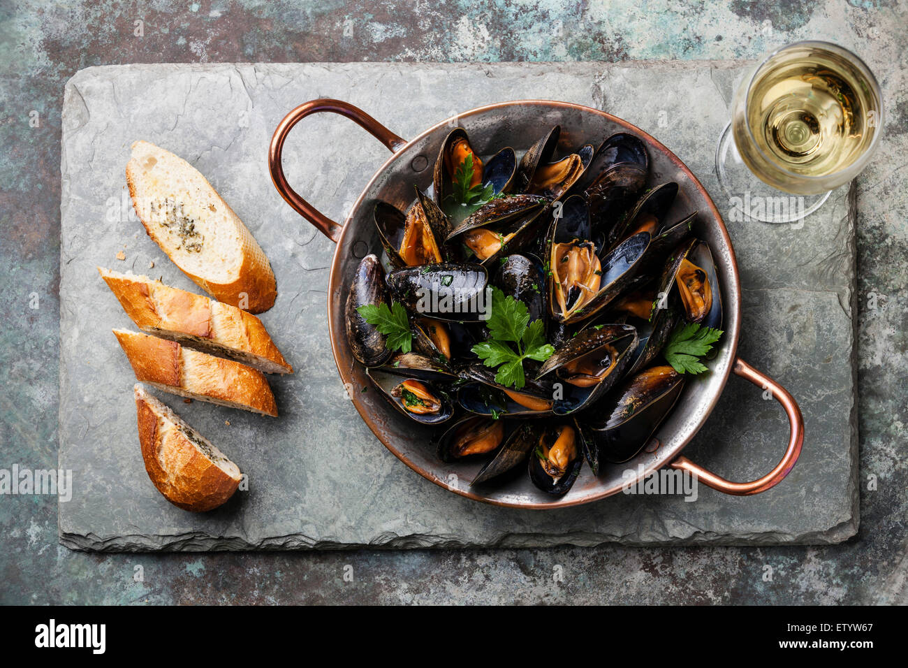 Muscheln in Kupfer Kochen Schüssel und französische Baguette mit Kräutern auf Stein Schiefer Hintergrund Stockfoto