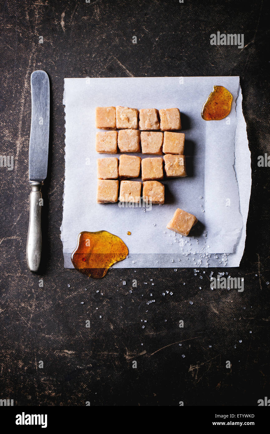 Fudge, Süßigkeiten und Karamell auf Backpapier, serviert mit Vintage Messer auf dunklem Hintergrund. Ansicht von oben Stockfoto