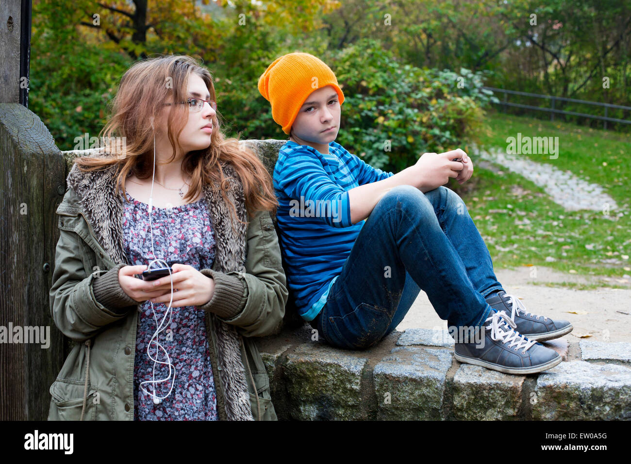 Teenager-Mädchen und ein Junge draußen in einem Park mit Handys Stockfoto
