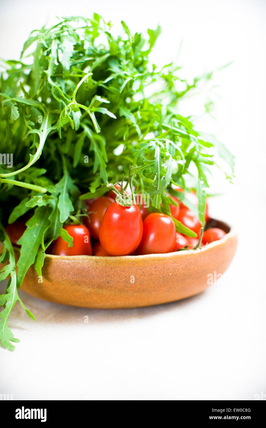 Grüner Salat und rote Tomaten roh auf Platte auf neutralem Hintergrund Detail mit selektiven Fokus Stockfoto