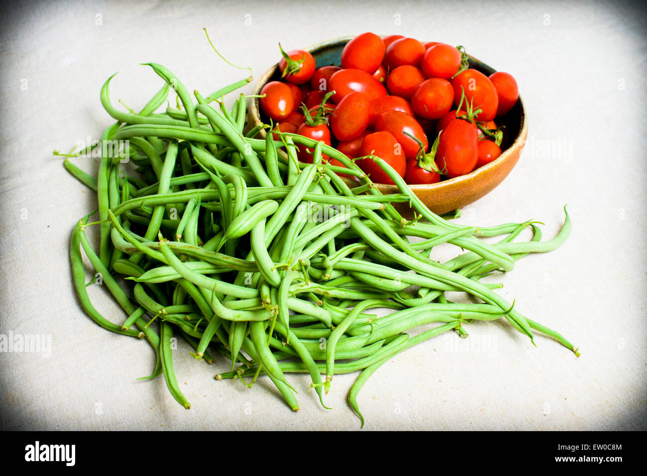Rohe grüne französische Bohnen und rote Tomaten auf Teller auf neutralem Hintergrund Stockfoto