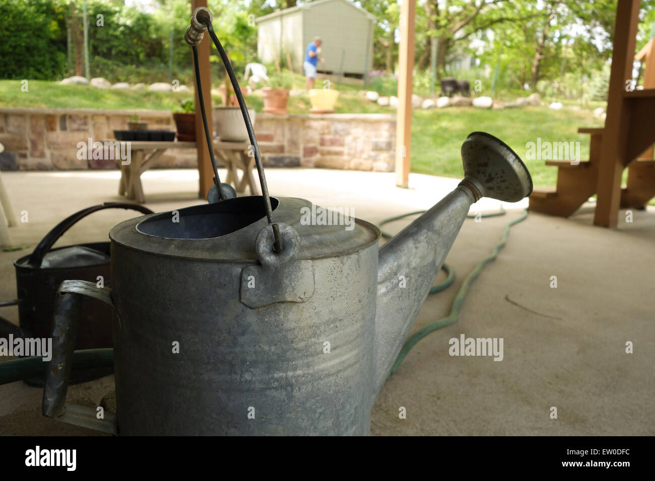 Aluminium-Gießkanne auf Veranda, im Vordergrund mit Mann im Hintergrund, die Arbeit im Garten. USA. Stockfoto