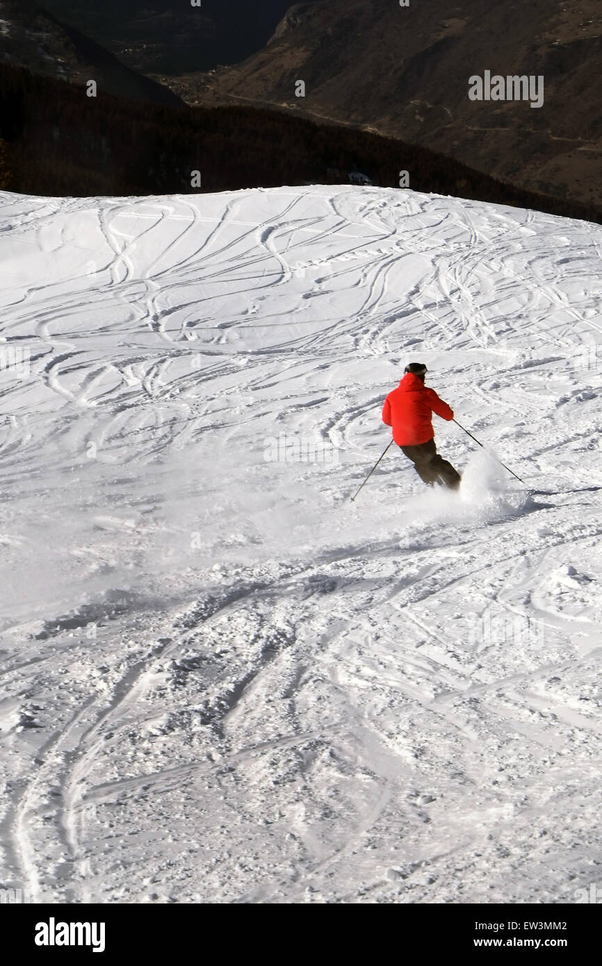 Ein Skifahrer in einer roten Jacke Powder-skiing in Richtung eines Tals von hinten gesehen Stockfoto